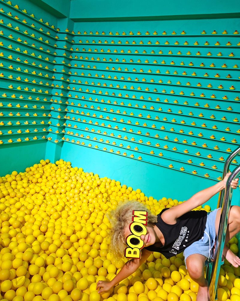 Keanu Tetteh lying in a yellow ball pit in a turquoise room