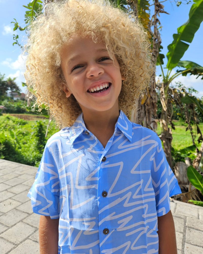 Keanu Tetteh laughing on a tropical path in a blue patterned shirt