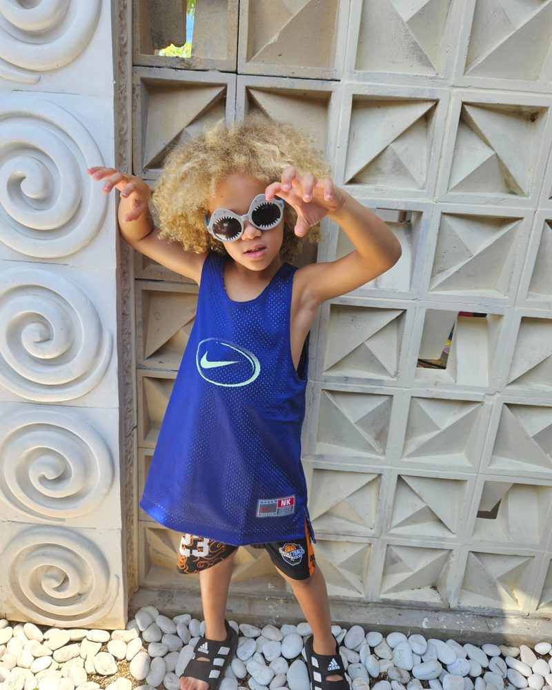 Keanu Tetteh in a blue sports vest and sunglasses against a patterned wall