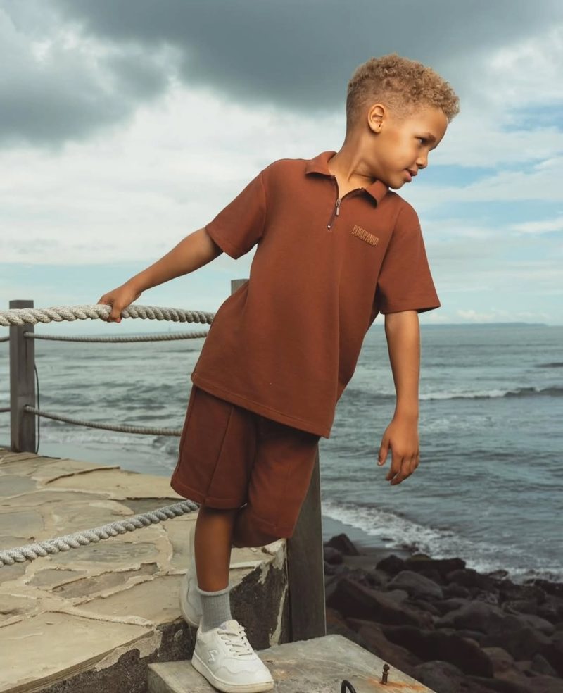 Keanu Tetteh in a brown co-ord outfit standing at a sea railing