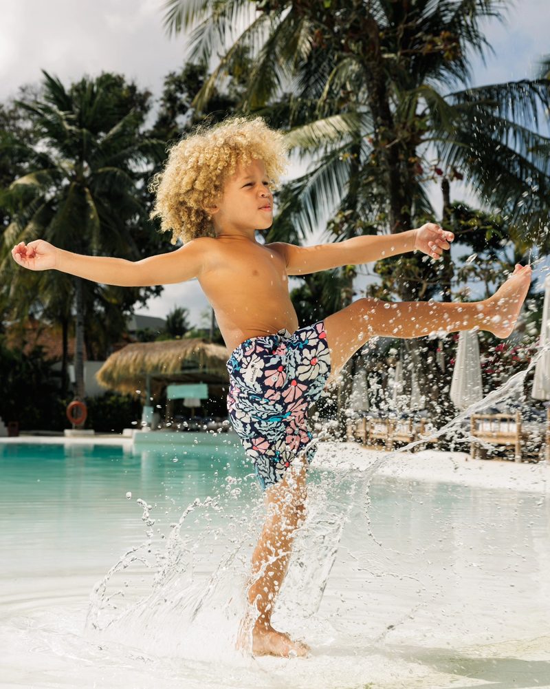 Keanu Tetteh kicking up water in a pool with palm trees behind