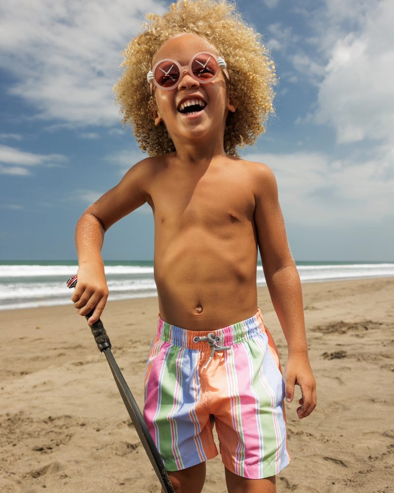 Keanu Tetteh laughing on the beach in rainbow swim shorts and sunglasses
