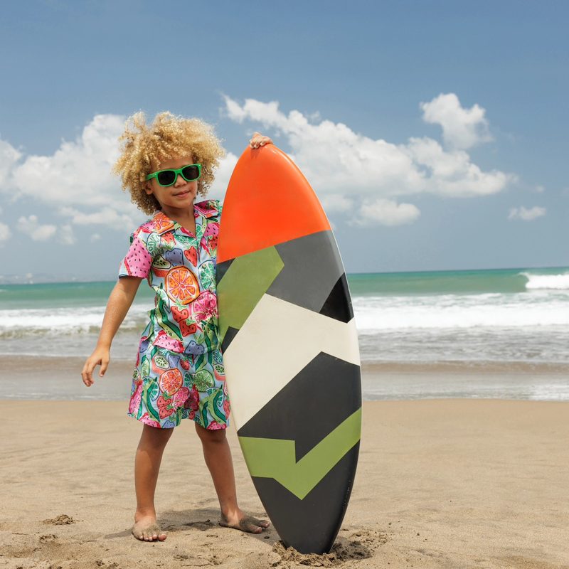 Keanu Tetteh on the beach with a surfboard, wearing a floral set and sunglasses