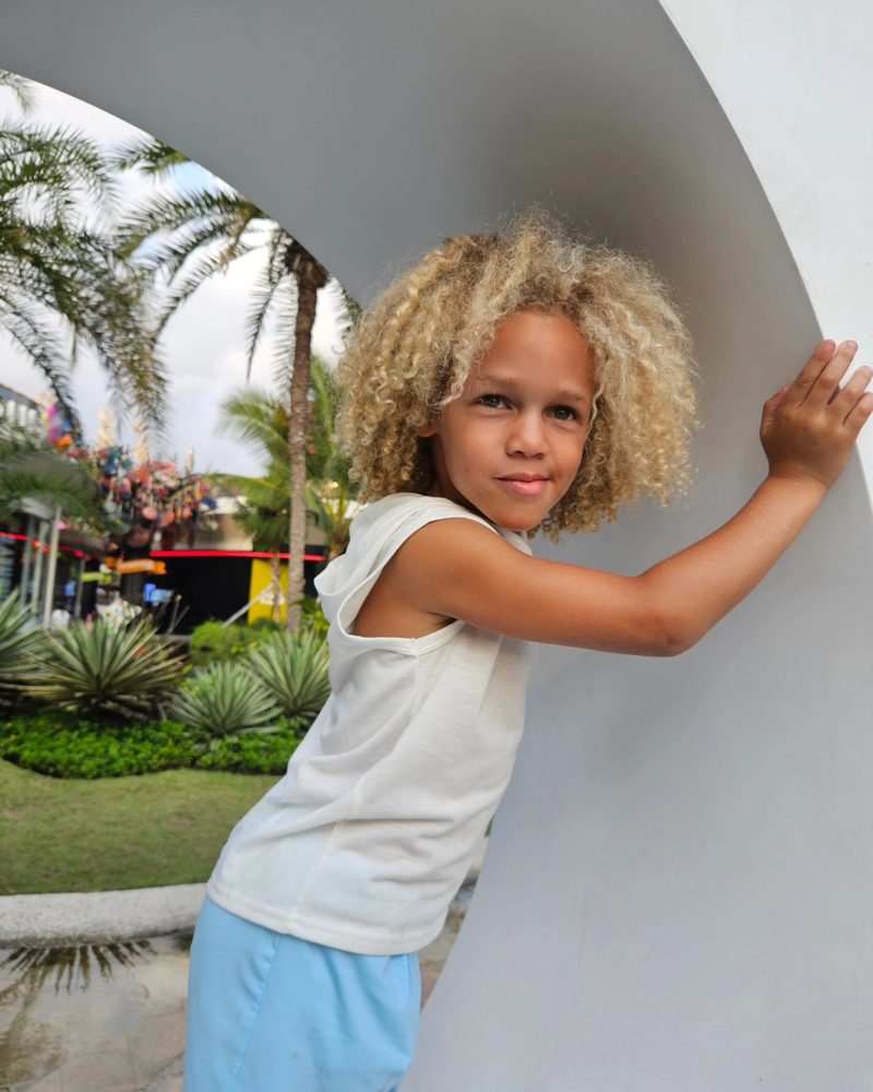 Keanu Tetteh leaning on a white sculpture arch in a tropical garden