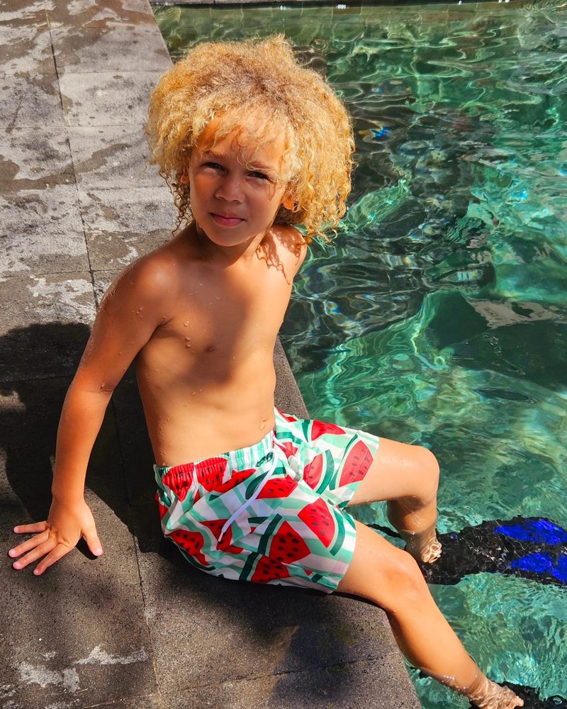 Keanu Tetteh sitting on a rock above clear water in watermelon print swim shorts